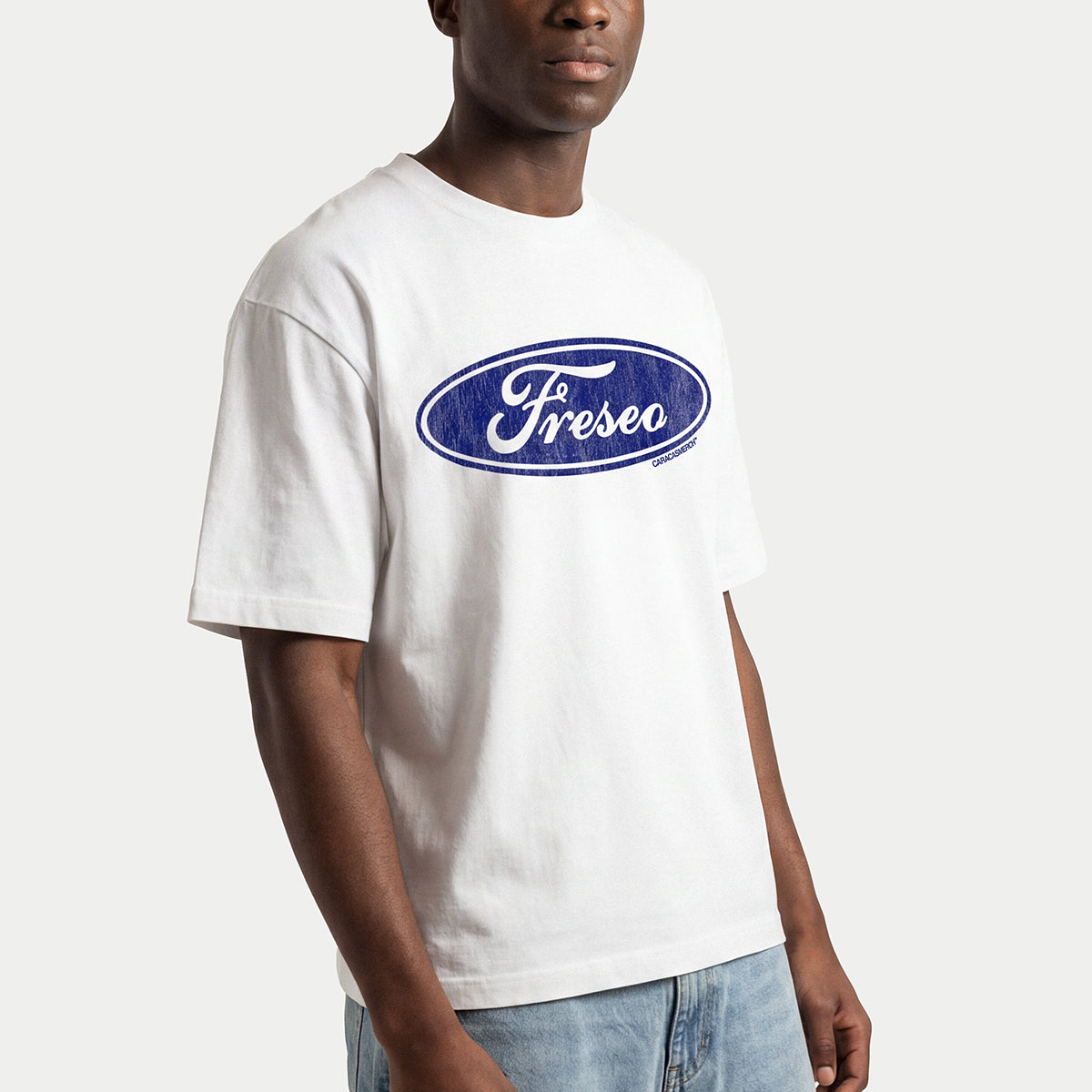 Primer plano de un hombre llevando la camiseta boxy blanca «Freseo» de Caracas Merch con el óvalo azul